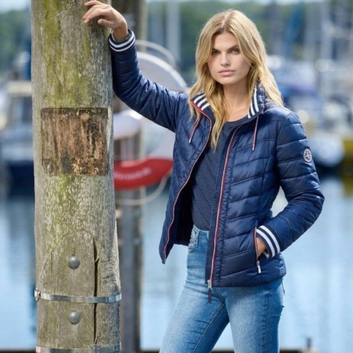 Dame i navy quiltet sommerjakke med stribede ribkanter ved havn, der viser sommerjakke trends for 2026
